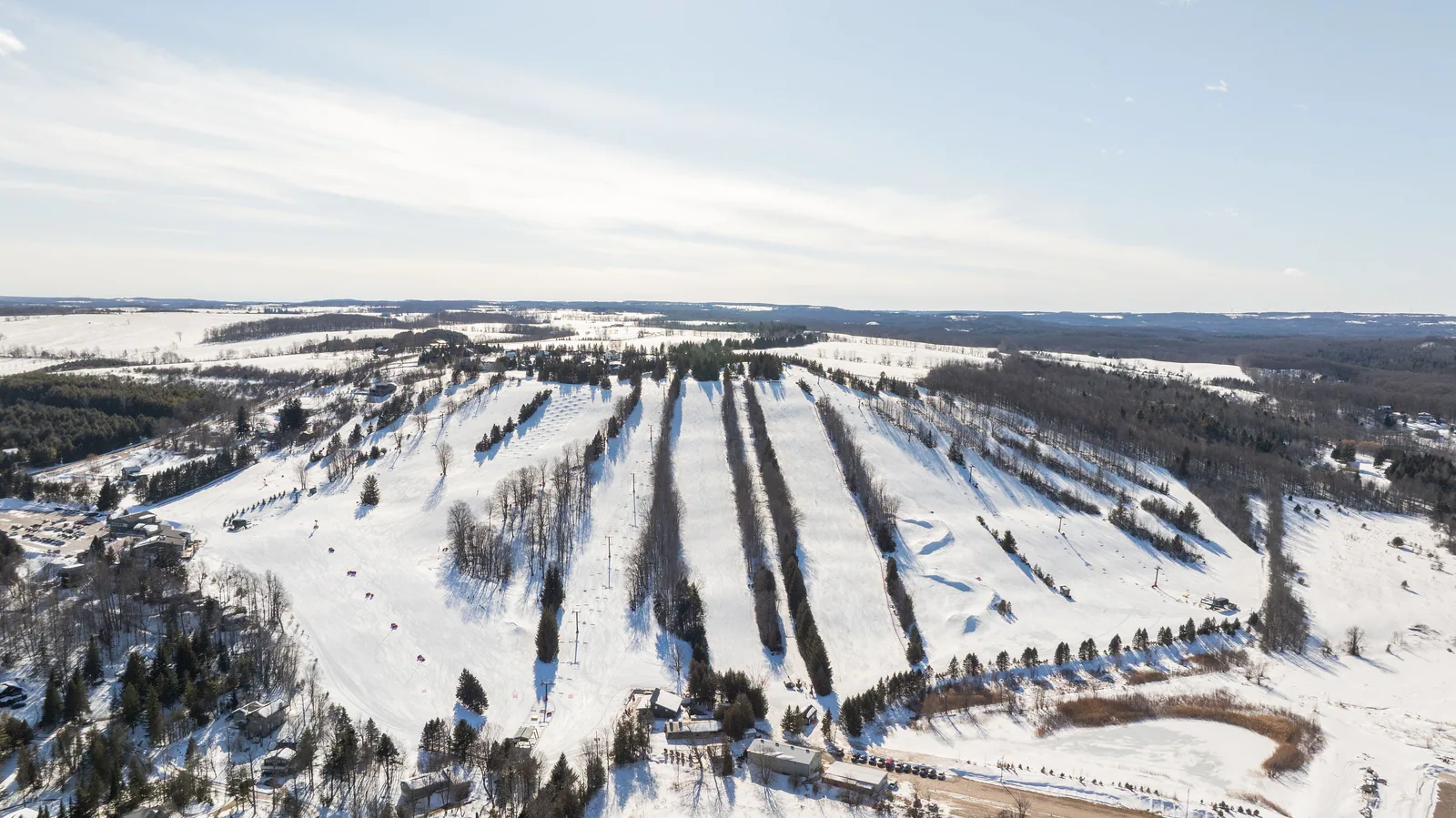 Aerial view of a snow-covered ski hill with pistes and surrounding pine forests
