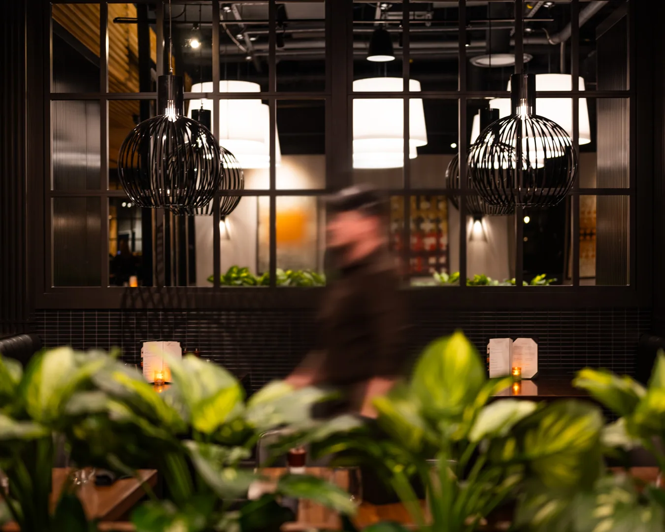 Milestones restaurant interior with modern lighting, blurred person, and plants in foreground