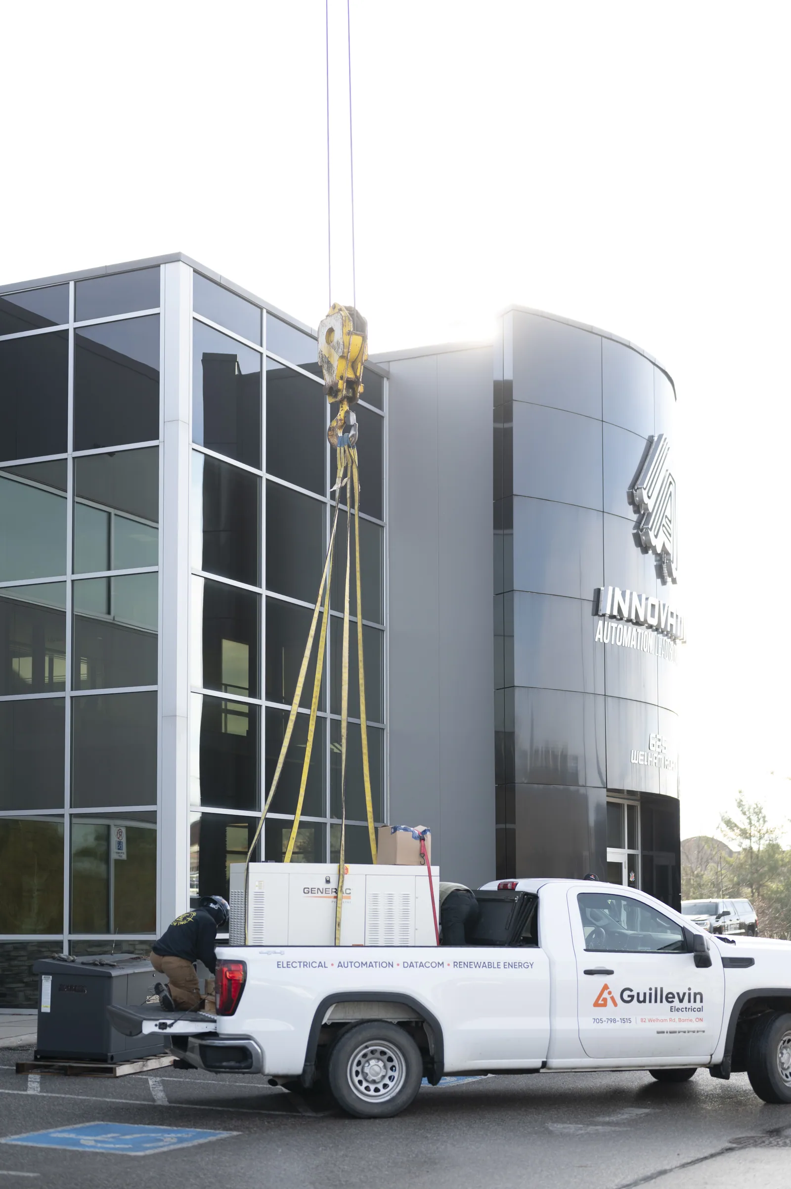 Worker near a truck and large generator being lifted by a crane at a commercial building