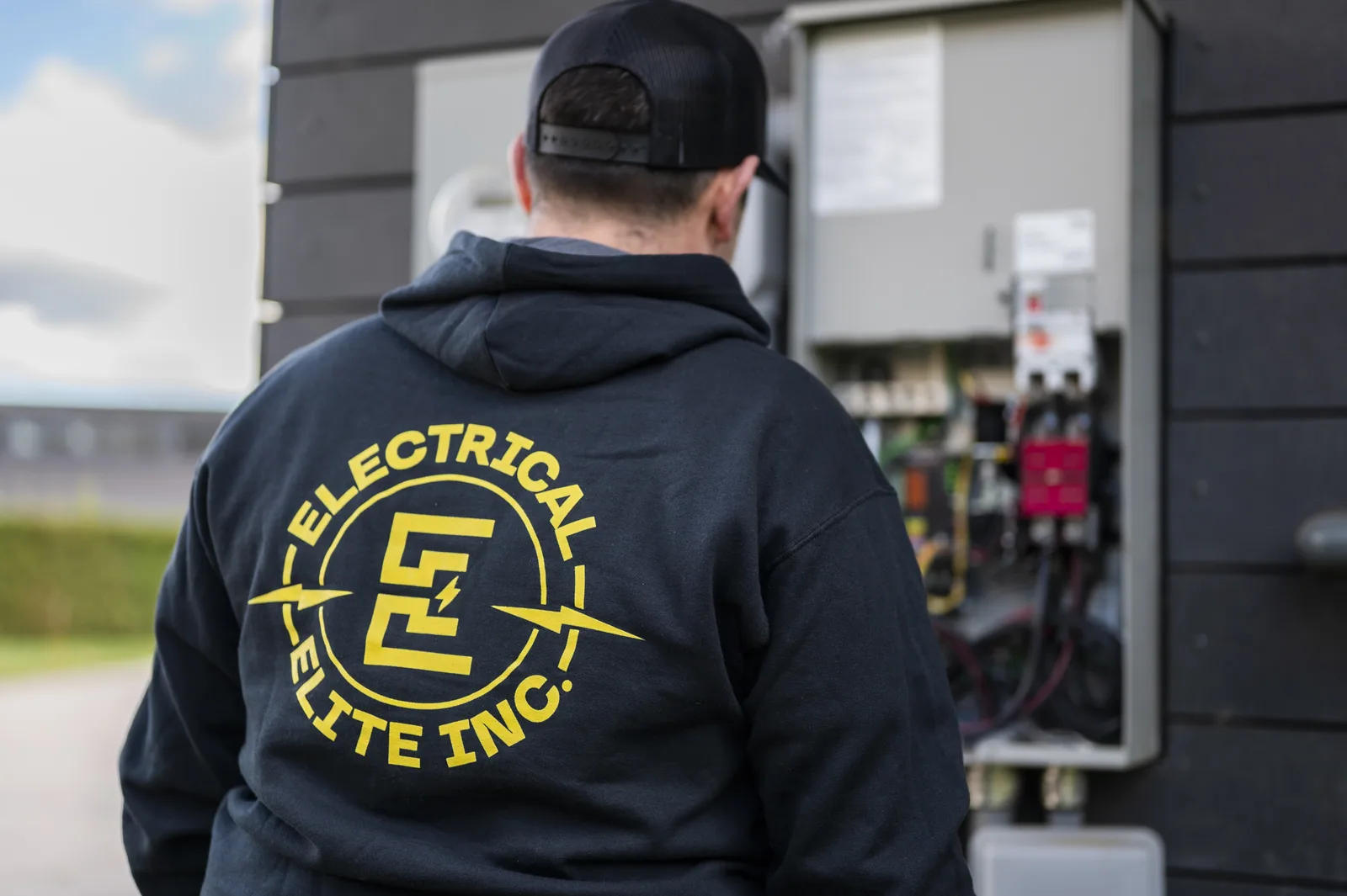 Electrician in black Electrical Elite hoodie inspecting an open electrical panel