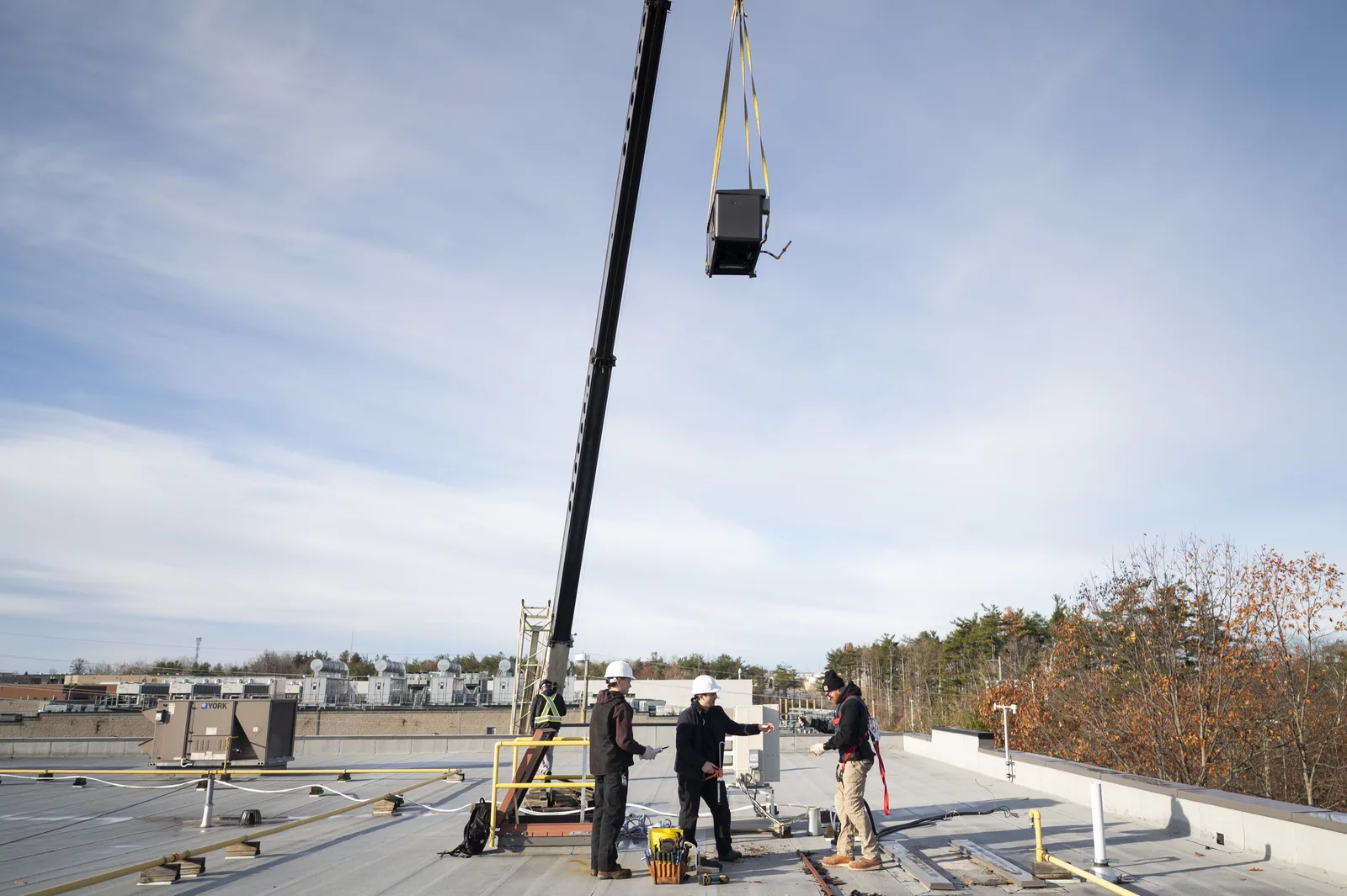 Construction crew on a rooftop, a crane lifting equipment against a clear sky