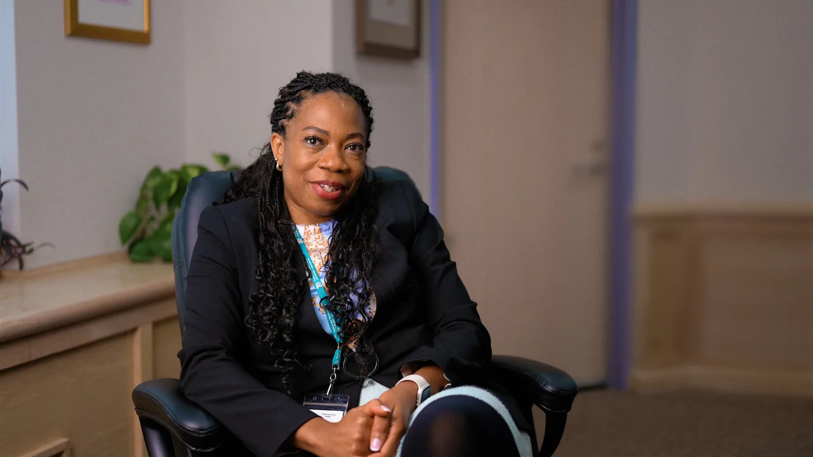 Black woman physician smiling in a hospital office setting, wearing an ID badge