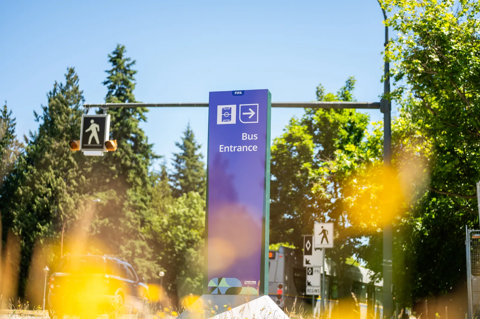 Tall purple FIFA World Cup signage for bus entrance, bright green trees in background